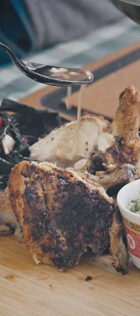 A mound of dark green kale salad, a grilled chicken leg, and a bowl of finely chopped sauce ingredients site side by side, ready to plate