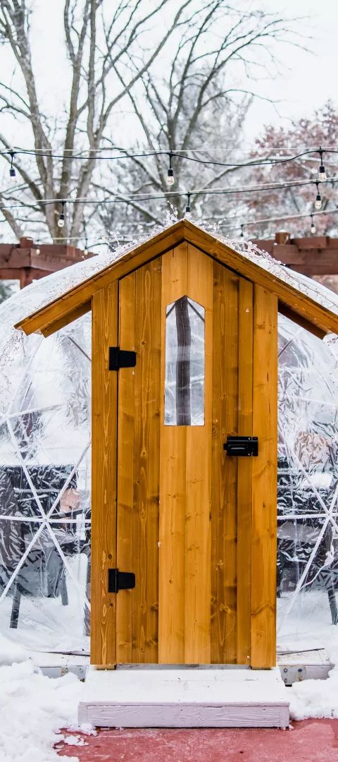 Three clear geodesic domes with wooden doors surrounded by snow